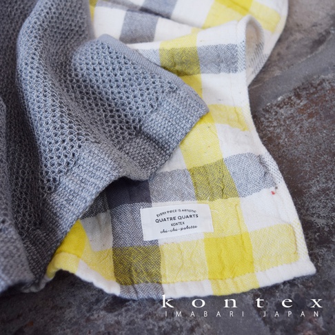 一款灰色的網狀織紋毛巾蓋在一條黃色和灰白色格紋的毛巾上，下方有一張標籤，上面寫著 KONTEX IMABARI JAPAN。