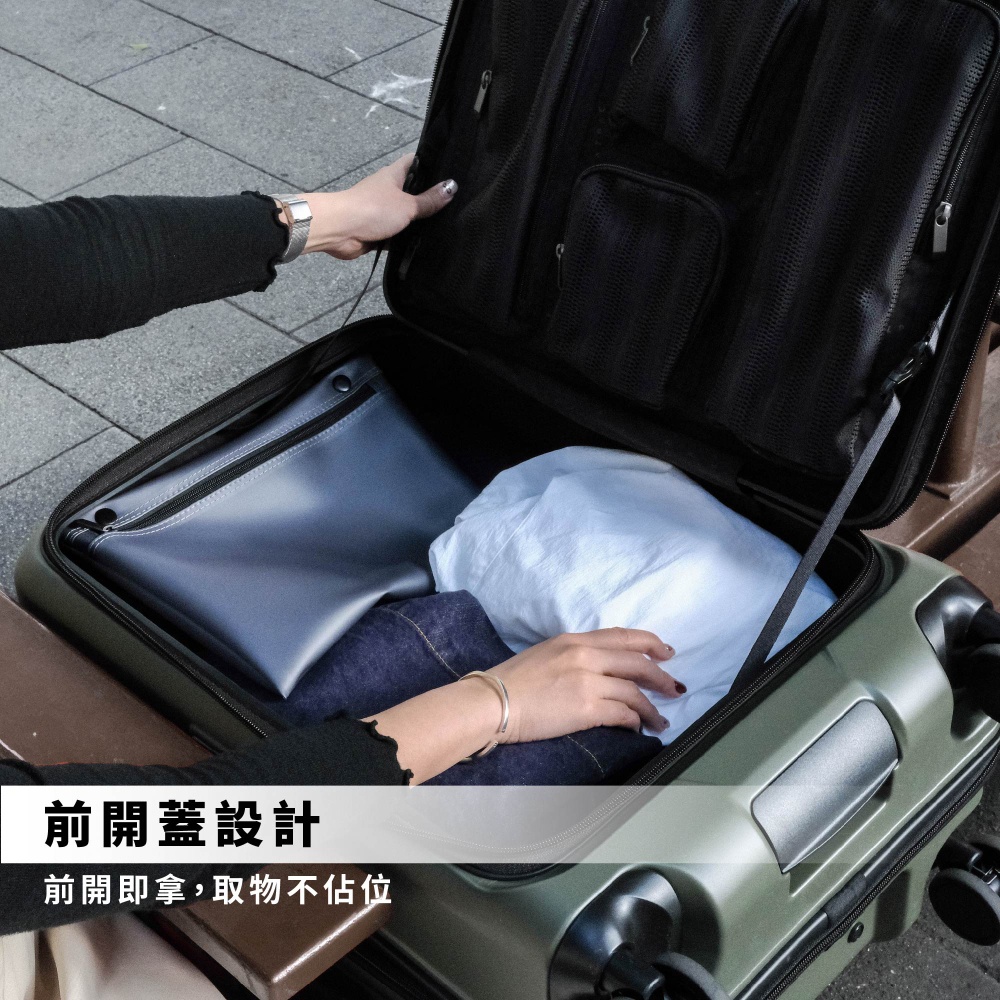 一位女性使用者正從橄欖綠色的AZPAC 25吋前開口行李箱中拿取物品，行李箱採用方便的前開蓋設計，箱內配置多層收納空間，呈現出俐落且便於隨時取物的商務旅行風格。