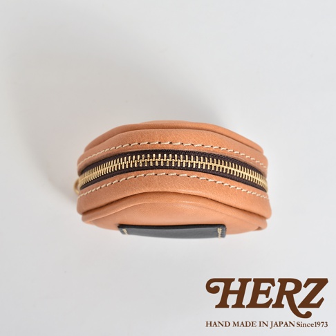 淺棕色皮革製成、飯糰造型的職人手作小物收納包，配有金色拉鍊及黑色皮革裝飾，縫線清晰可見。