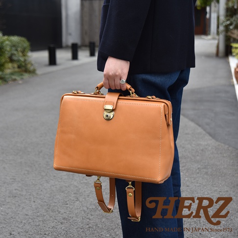 職人手作皮革軟式杜勒斯三用背包，採用淺棕色皮革，帶有金色鎖扣和可拆卸肩帶。