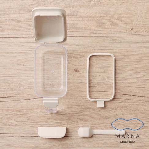 這張俯視照片展示了 MARNA 品牌的透明密封調味料盒拆解零件，包括透明盒身、開蓋扣環、防潮密封圈、蓋子與專用量匙，呈現為奶油白色系的簡約廚房收納用品，並在右下角標示了品牌標誌與創立年份。