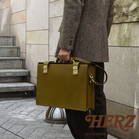職人手作皮革兩用機師箱，olivine 綠色，配有金色鎖扣和可拆卸肩帶，展現精緻工藝。
