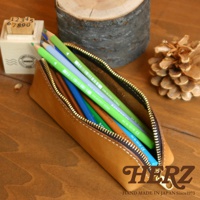 職人手作皮革三角收納筆袋，淺棕色皮革，內含多色鉛筆，金屬拉鍊，簡約設計。