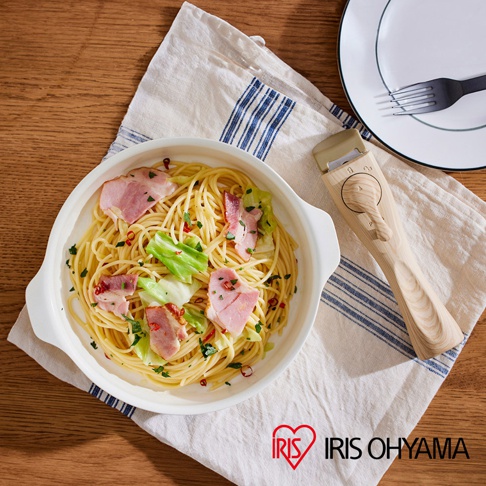 白色陶瓷不沾平底鍋盛著培根高麗菜義大利麵，旁邊放著木質手把的可拆卸鍋蓋，上方有藍色條紋的白色布巾，右側為白色盤子和黑色叉子。