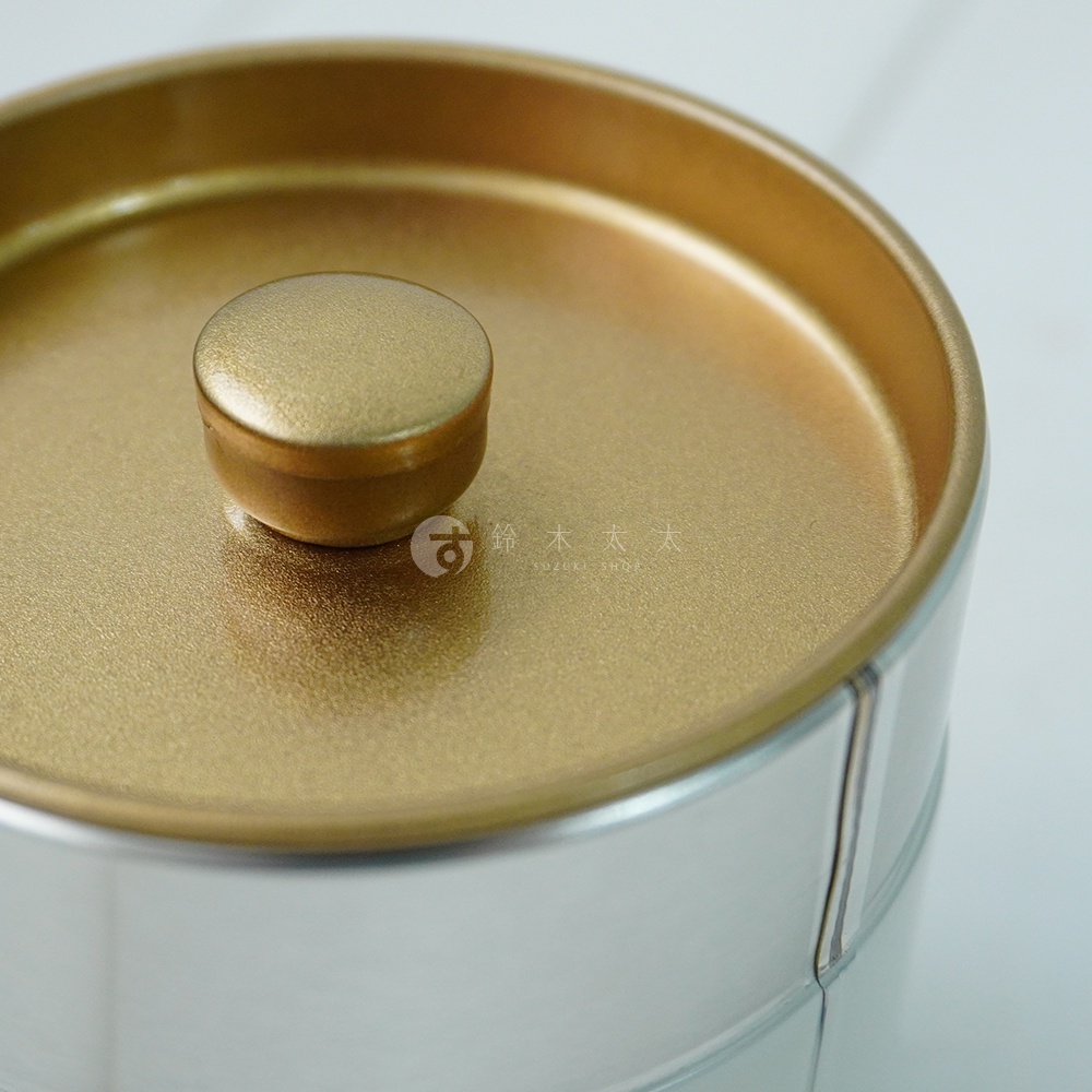 簡約錫製茶葉罐，頂部為金色圓形旋鈕，罐身為銀色，表面光滑，適合儲存100克茶葉，具有氣密防潮功能。