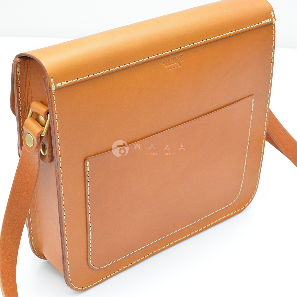 職人手作皮革經典厚實單肩包，淺棕色皮革，正面有一個方形外袋，袋口有金屬釦環，縫線明顯，品牌Logo印製於袋蓋內側。