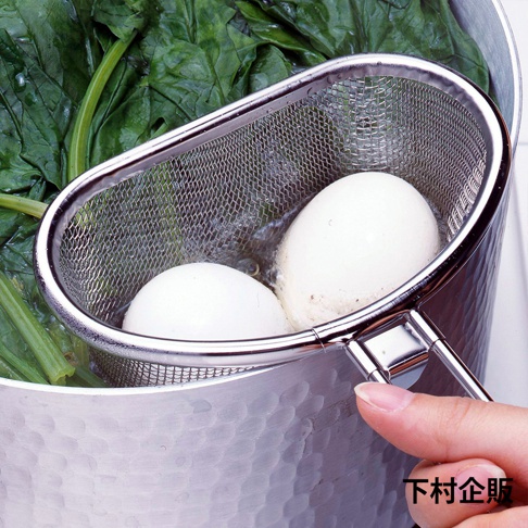 不鏽鋼可掛式料理濾網，帶有細網篩，內有兩個白色水煮蛋，置於熱水中，背景為綠色蔬菜。