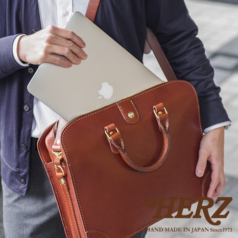 職人手作的棕色皮革公事包，可放入筆記型電腦，配有提把與可調式肩帶。