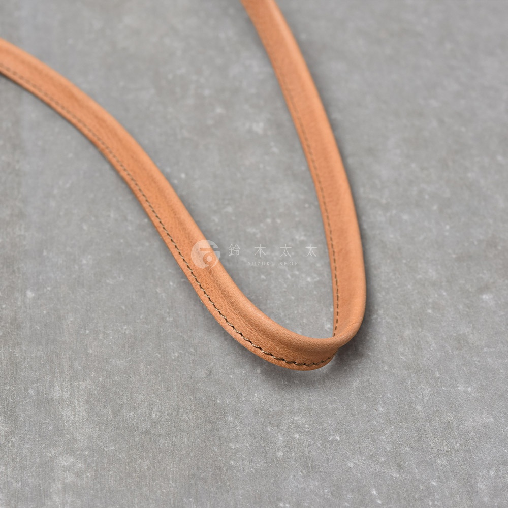 淺棕色皮革製成的包包提把，細緻車縫線，背景為灰色紋理桌面