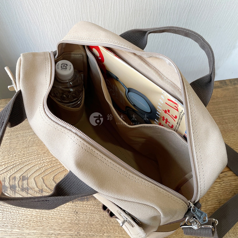 米色純棉帆布側背包，內部裝有水瓶、雜誌和一副耳機。