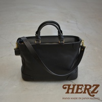 黑色皮革製成的職人手作Organ兩用商務托特包，配有雙提把和可拆卸肩帶，金色五金件，底部有保護角，整體設計簡約。