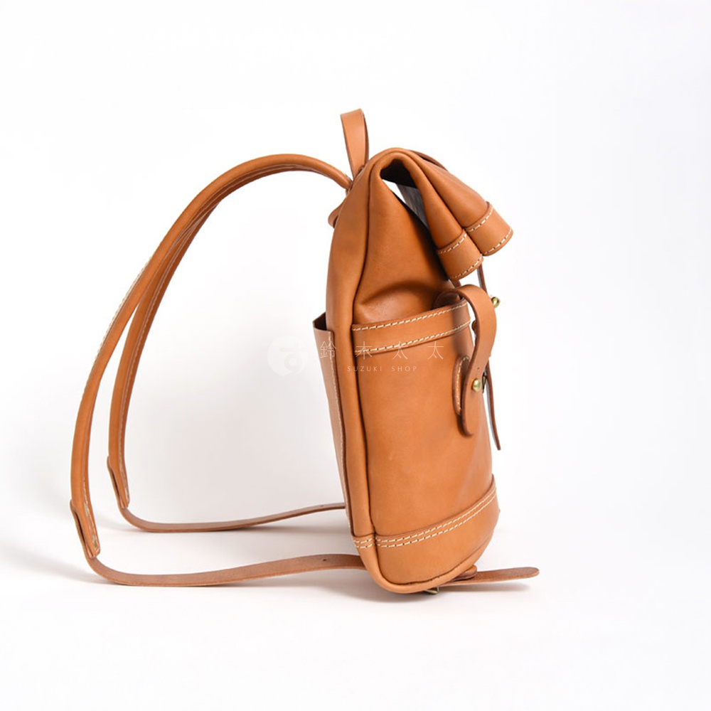 一件棕褐色皮革雙口袋折蓋後背包，配有可調節的肩帶和金屬扣環，側面有一個開放式口袋，縫線精緻。