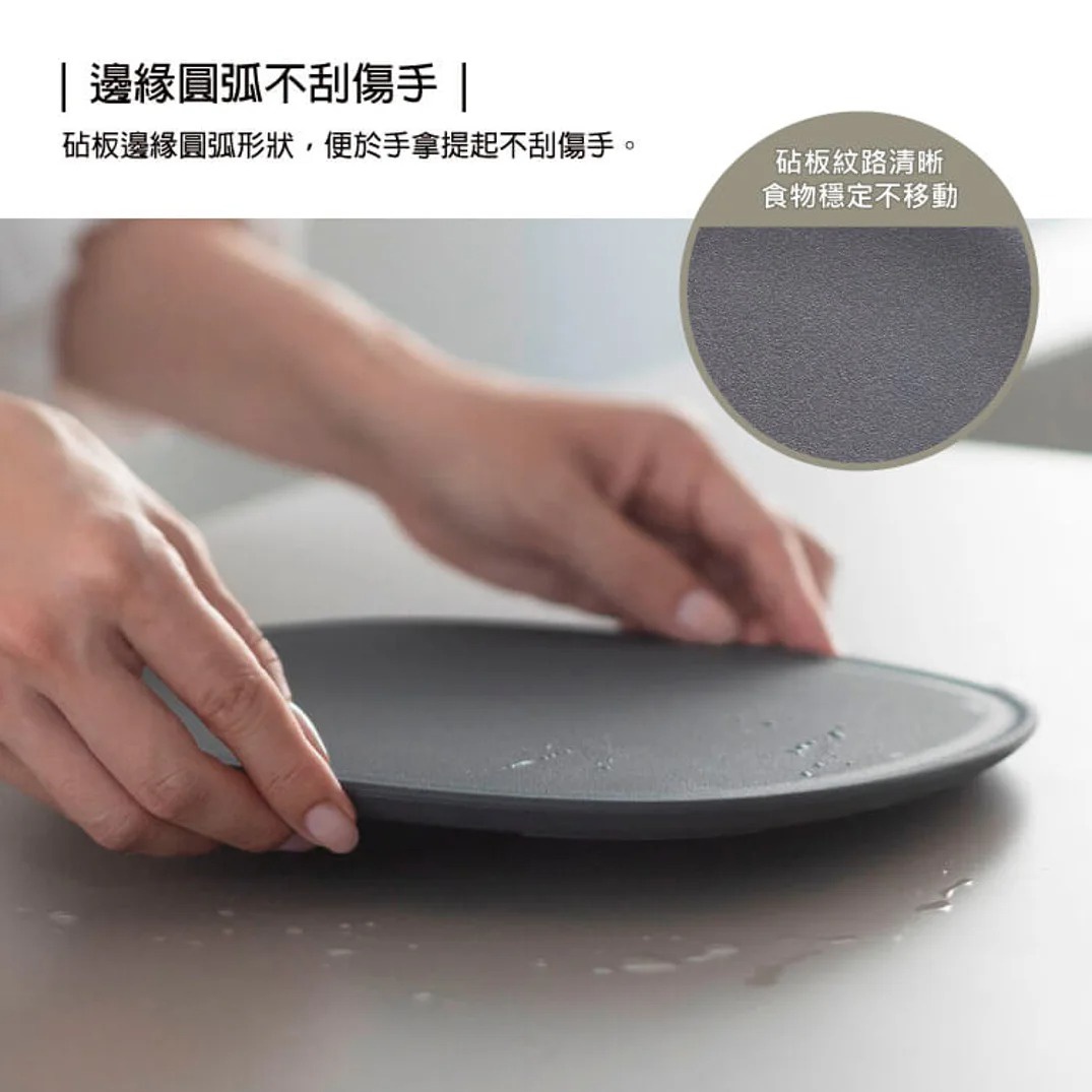 一雙手正將一個光滑的圓形深灰色砧板放在廚房檯面上，砧板邊緣帶有圓弧形設計，確保手部握持安全且不刮手，上方的文字標示其「邊緣圓弧不刮手」。