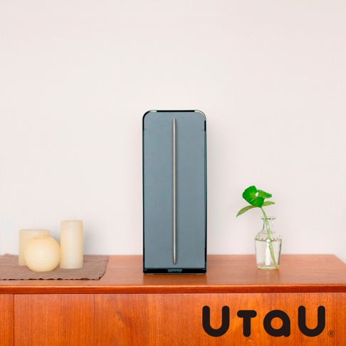 一個灰色直立式收納整理櫃，櫃面中央有一條銀色長形裝飾條，櫃子左側擺放著兩個白色圓柱狀蠟燭和一個橘黃色圓球狀蠟燭，右側擺放著一小株綠葉植物在玻璃瓶中，整體置於木質櫃台上。