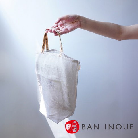 提把式麻布收納袋，米白色，質感透氣，有黃色與藍色條紋的織帶提把，袋身線條簡潔，適合收納蔬果。