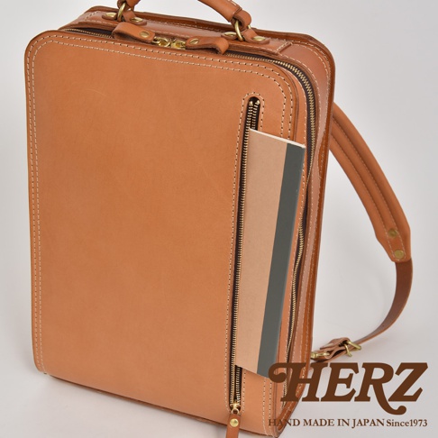 職人手作皮革商務電腦後背包，採用天然皮革材質，經典棕褐色。包款設計簡潔，前方有拉鍊口袋，側面可見筆記本。做工精緻，縫線清晰，質感優良。