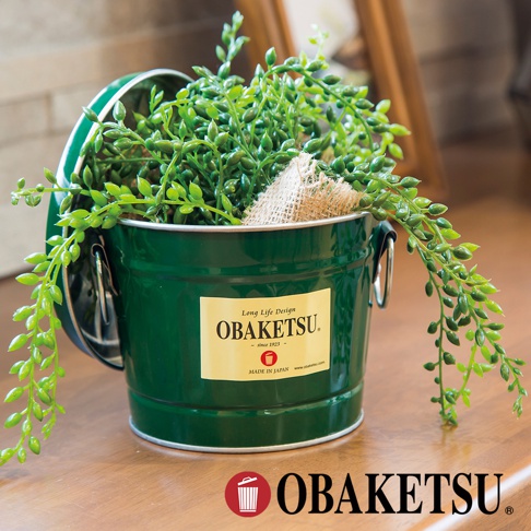 OBAKETSU 手工製多功能迷你桶，綠色金屬桶身，盛裝著垂墜的綠色植物，桶身貼有 OBAKETSU 品牌標籤。