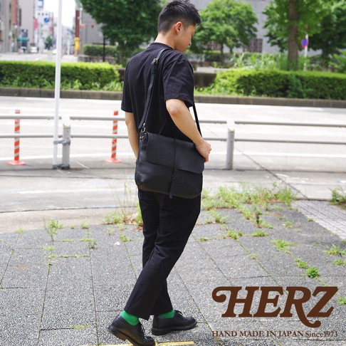 一名男子背著黑色的HERZ皮革馬鞍包，走在街道上。