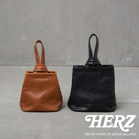 職人手作皮革Organ單柄手提包，左為棕色，右為黑色。兩款包皆為方形設計，頂部有單一皮革提把，以繩結固定。材質為皮革，質樸自然。