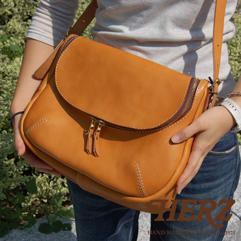 日本HERZ手工皮革大容量馬鞍包，焦糖色，採用拉鍊開合，由一位女士展示。