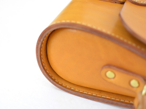 職人手作皮革寬扣帶馬鞍包 (CP-1)，採用淺棕色牛皮材質，縫線整齊，包包邊緣圓潤，帶有金屬卯釘裝飾。