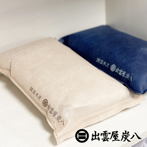 兩個長方形的調濕木炭包，一個為米白色，表面有網狀紋理，印有「調濕木炭」及品牌標誌；另一個為深藍色，同樣印有品牌標誌。