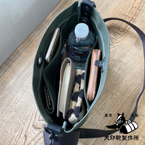 綠色純棉帆布迷你側背包，內部裝有手機、筆記本、水瓶、錢包和一條豹紋圍巾。