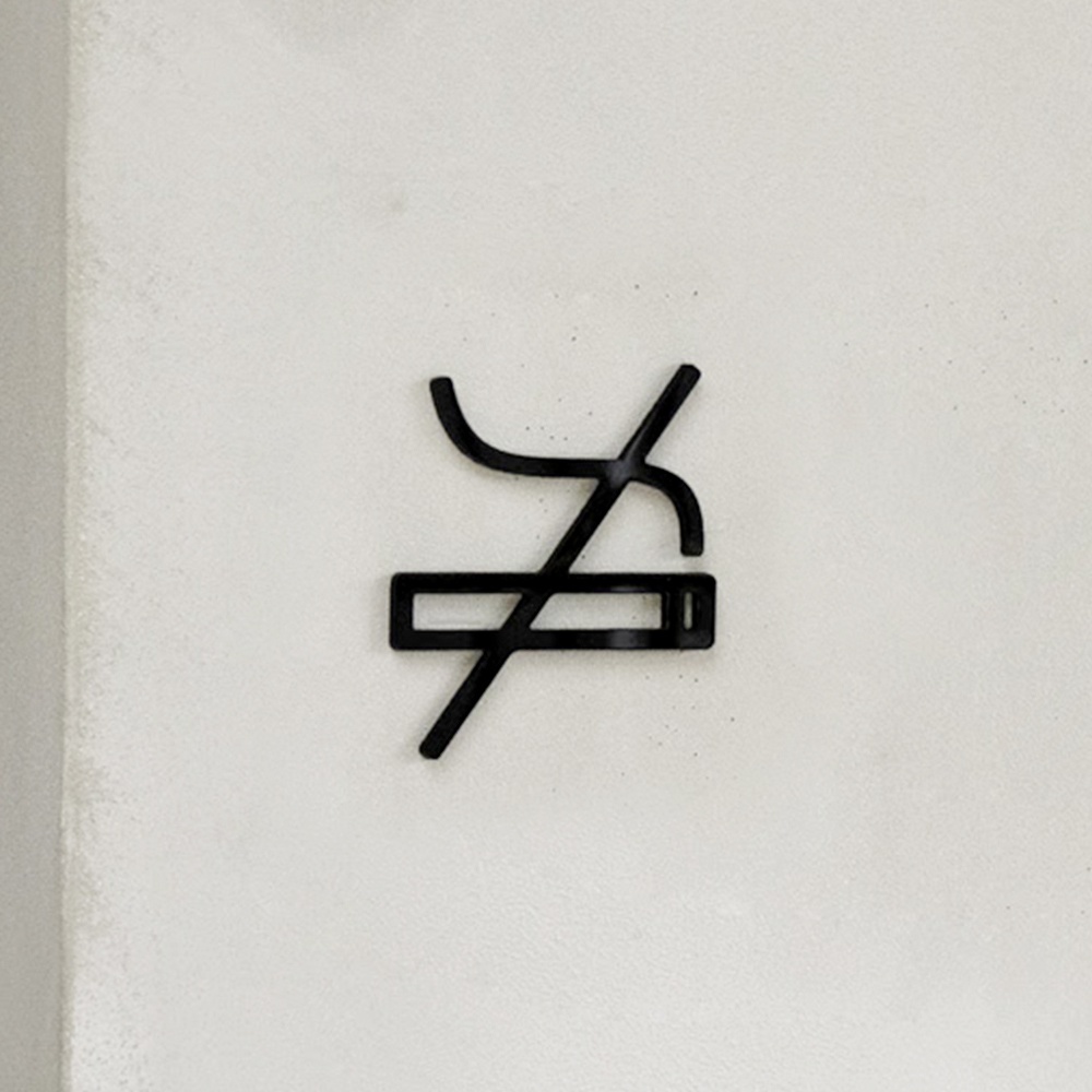 黑色金屬材質的「禁止吸煙」標誌，由一個香煙圖案加上斜線組成，安裝在淺色牆面上。