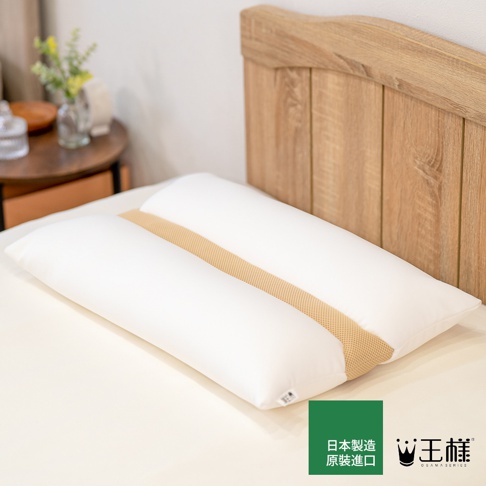 一個帶有品牌標誌和日文文字的白色枕頭，放在床上，背景是木製床頭板