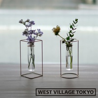 兩個黃銅金屬框架內置圓柱形玻璃水瓶，左側玻璃瓶內有紫色小花，右側玻璃瓶內有枯萎的黃色玫瑰和綠色枝葉。