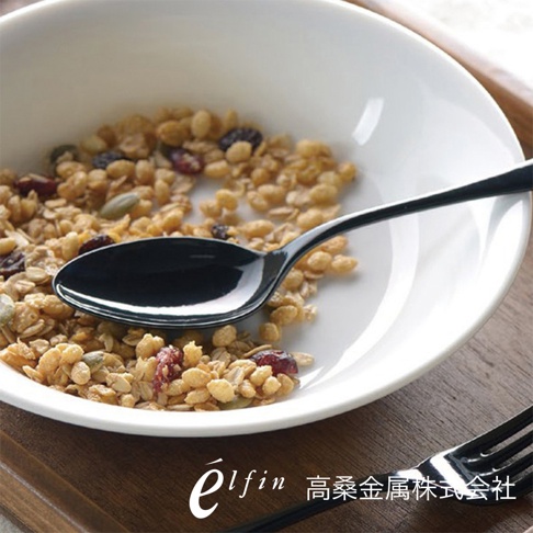 一個黑色的琺瑯餐匙，置於裝有燕麥片、堅果和果乾的白色碗中。