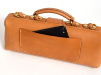 職人手作皮革橫長形杜勒斯單肩包，採用自然色澤的皮革製成，包身線條簡潔，配有黃銅扣環和手提把。前方有一個方便放置手機的外插袋，袋口飾有白色縫線。