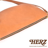 HERZ 職人手作皮革半圓馬鞍包，側面特寫，展示精緻縫線和拉鍊細節，下方印有品牌標誌。