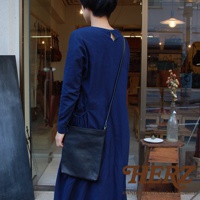 一位女性穿著藍色連衣裙，斜挎一個黑色皮革肩背包。包包為方形設計，材質柔軟，肩帶細長。