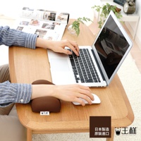 棕色布面減壓護腕枕，放置在木質桌面上，支援使用滑鼠的手腕，一旁有筆記型電腦和雜誌。