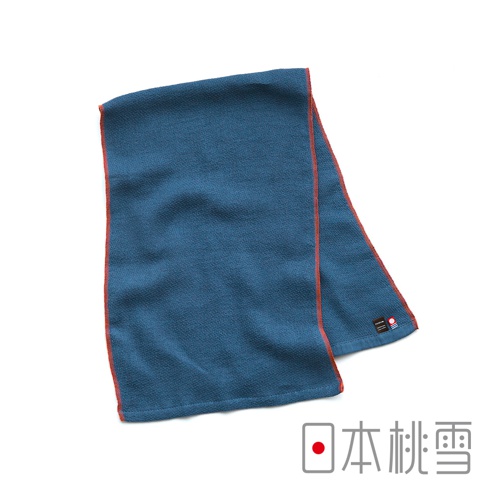 一張深藍色的日本桃雪 NUGUW 今治輕量快乾運動長毛巾，表面呈現細緻的毛圈質感，邊緣以顯眼的橘紅色縫線修飾，右下角配有品牌專屬的小巧織標，整體設計簡約且具有運動風格。