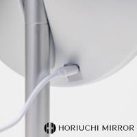 銀色金屬支架連接至白色圓形化妝鏡背面，一條白色充電線插入鏡背右側的充電孔。