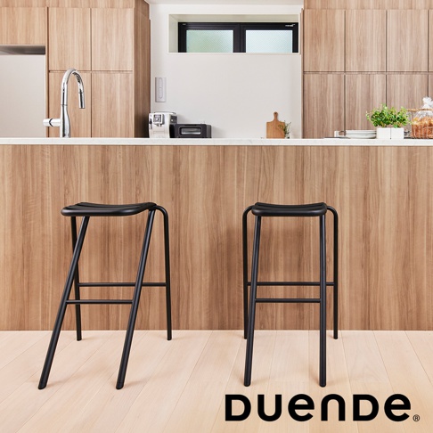 兩張黑色金屬吧檯椅，椅面為弧形凹槽設計，椅腳為細長金屬管構成，椅面與椅腳皆為黑色。