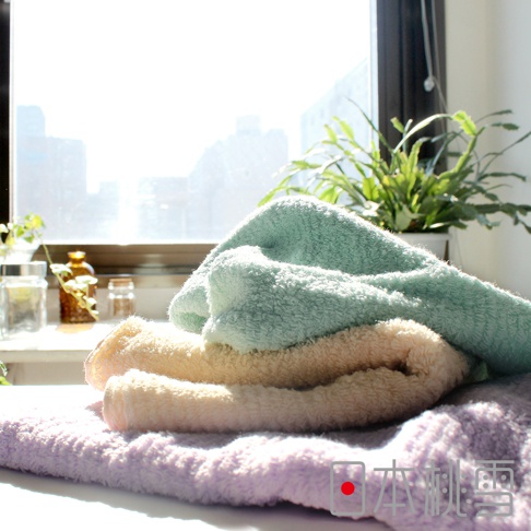 疊放的今治細絨浴巾，顏色由上至下為淺綠、淺黃、淺紫，質地柔軟，背景為窗戶和綠色植物。