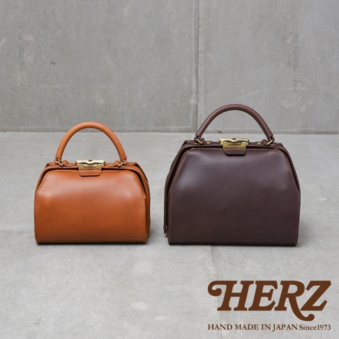 兩只職人手作皮革Organ兩用口金手提包，一為棕褐色，一為深棕色。兩款包皆為方形提把設計，配有金色口金開合，展現經典復古風格。