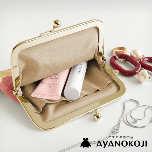 品牌AYANOKOJI的金色口金包內放著兩支唇部保養品，旁邊擺著樹脂項鍊和銀色項鍊，背景為白色。