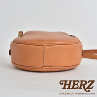 淺棕色皮革小圓包，側面視角，包身圓潤飽滿，縫線精緻，搭配皮質提把與肩帶。