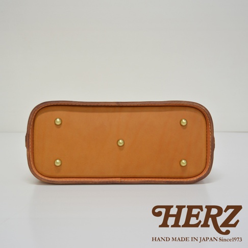 職人手作皮革長型迷你醫生包 CW-106，展示其底部，採用天然皮革材質，呈現溫潤的棕褐色，四角設有金色金屬腳釘，邊緣使用細緻縫線處理。