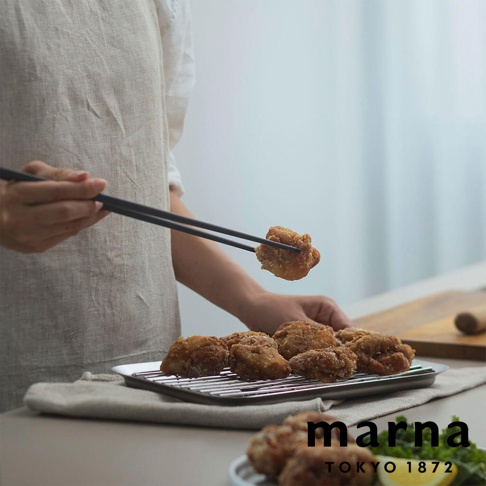 主體為炸雞塊，其中一塊正被黑色筷子夾起，下方盤子裡也擺放著多塊炸雞塊，圖片右下角印有「marna TOKYO 1872」的文字。