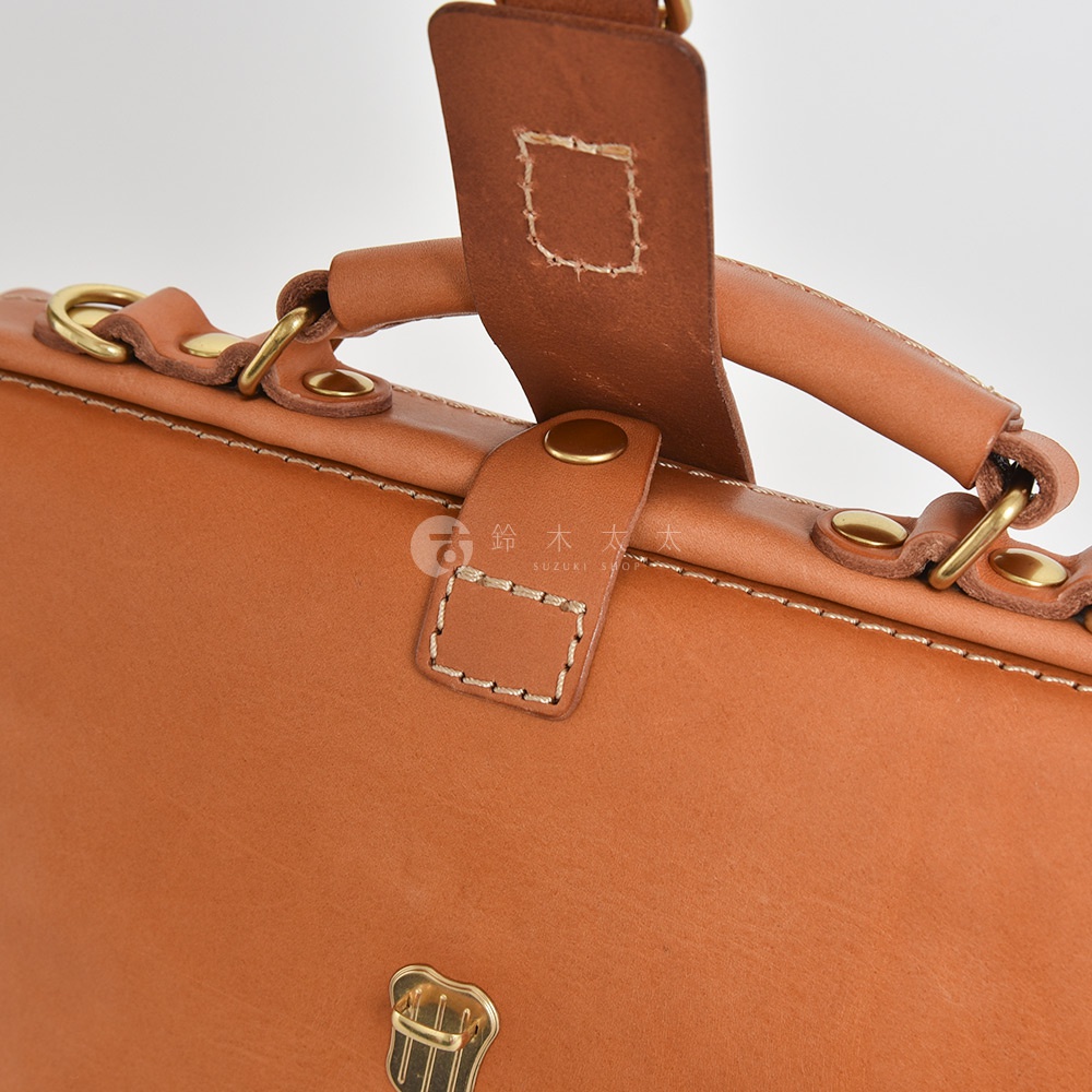 職人手作的淺棕色皮革迷你包，展示了包的頂部結構、皮革提把、金屬釦件及縫線細節。