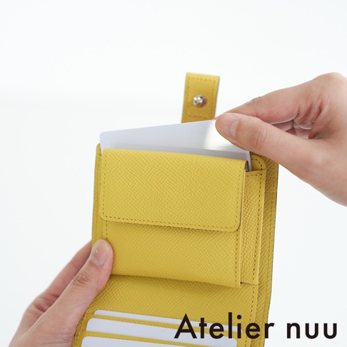 Atelier nuu 品牌黃色皮革對折短夾，特寫鏡頭展示有人手正在將卡片放入夾層。