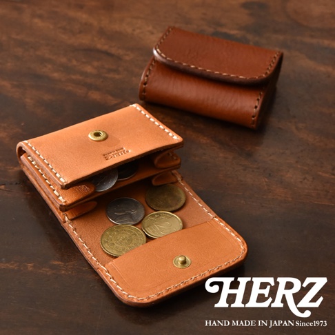 深褐色手工縫製的日本HERZ皮革雙折零錢包，一個展示閉合狀態，另一個則展開平放於木質桌面上，內部整齊擺放著多枚不同尺寸的硬幣，整體呈現出經典簡約的職人皮件質感。