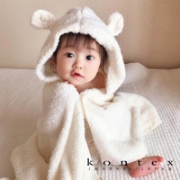 一名嬰兒裹著一件厚實、柔軟的白色連帽浴巾，浴巾上有可愛的兔耳朵設計。