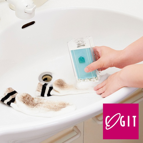 透明塑膠盒裝有藍色洗衣皂，一隻手持著，另一隻手正在用它清潔帶有黑色條紋的白色髒襪子。