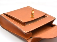 職人手作皮革單肩包，呈現天然棕色皮革，帶有細緻的縫線裝飾，包蓋上有一個金色金屬旋轉鎖扣。